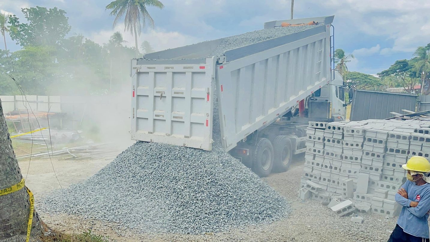 Dump truck unloading gravel aggregates beside stacks of hollow blocks