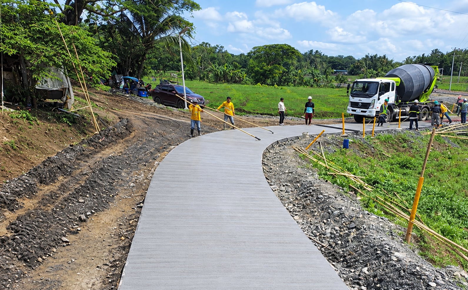 Crew finishing a curved concrete road, with a mixer truck behind
