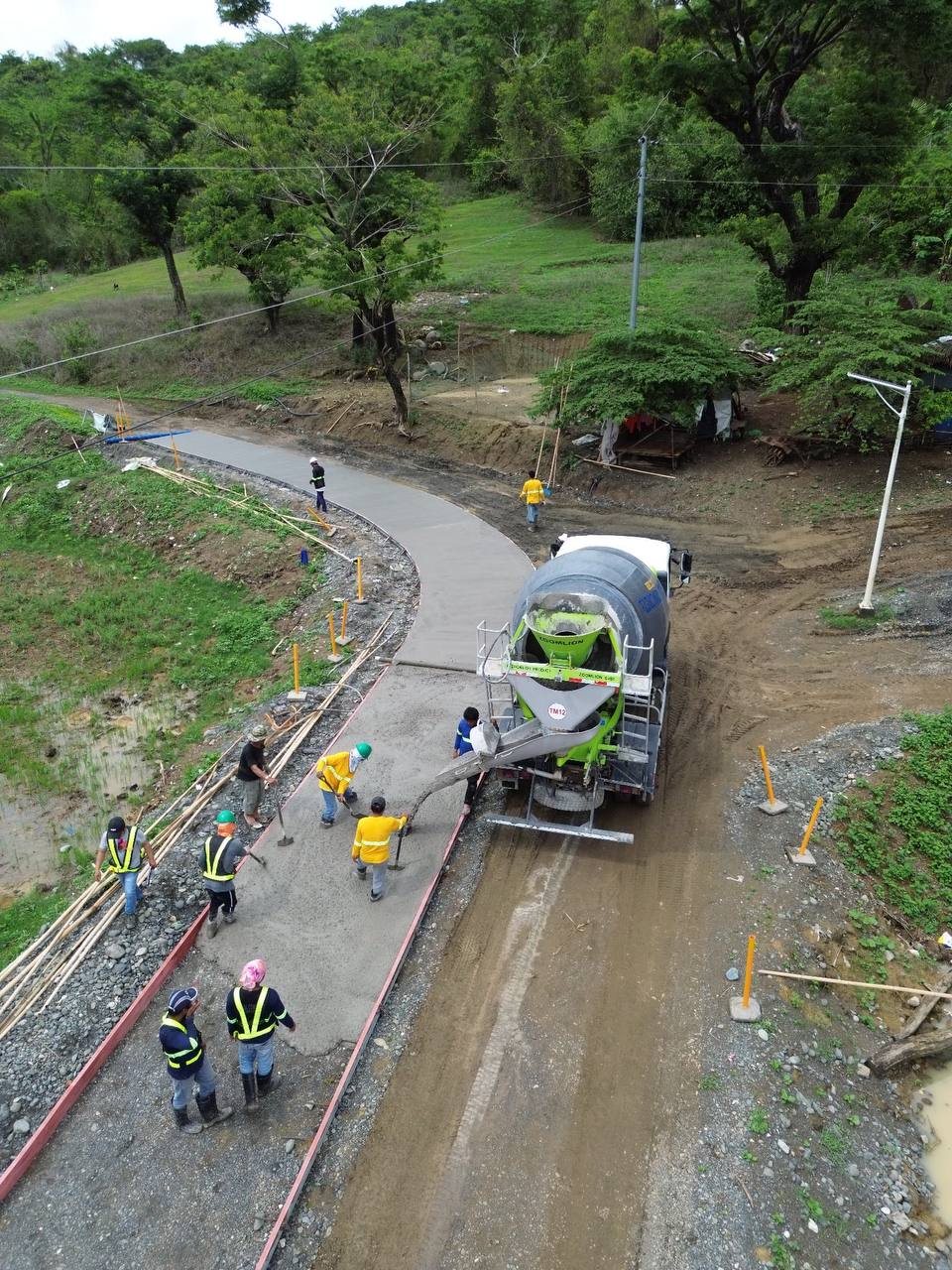 Mixer truck placing concrete for a road while a crew spreads it